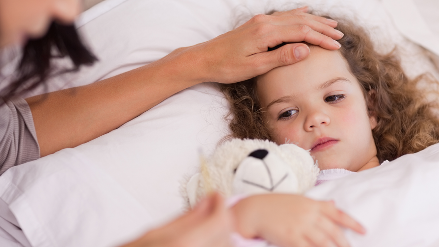 Kind ist krank und liegt mit Teddy im Bett. Mama prüft ihre Temperatur. 