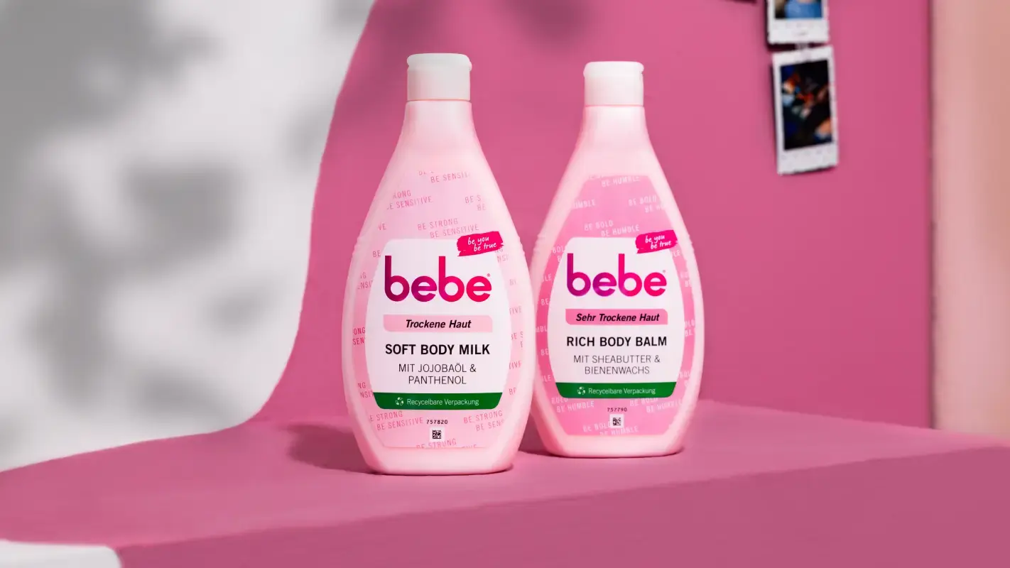 Bebe Produkte Soft Body Milk und Rich Body Balm stehen aufgereiht vor pinkem Hintergrund.