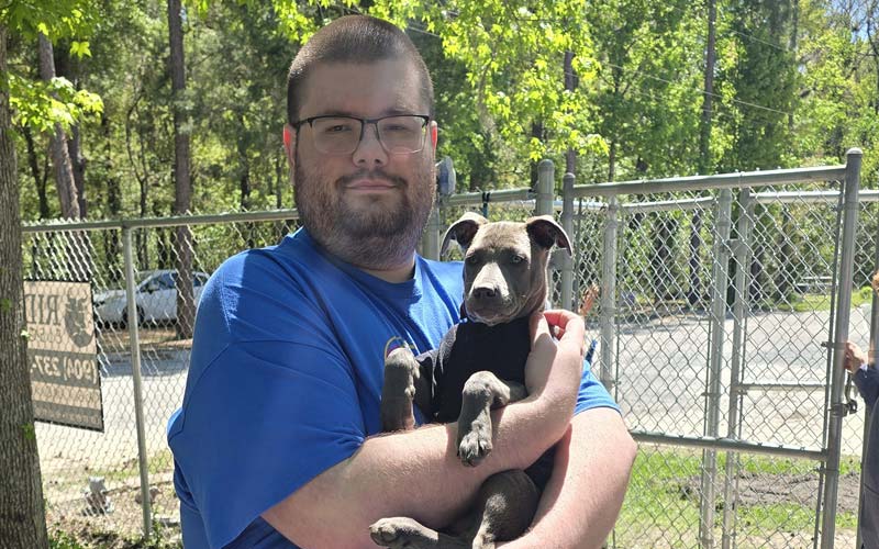 A photo of William holding a small dog in his arms at SAFE Animal Shelter