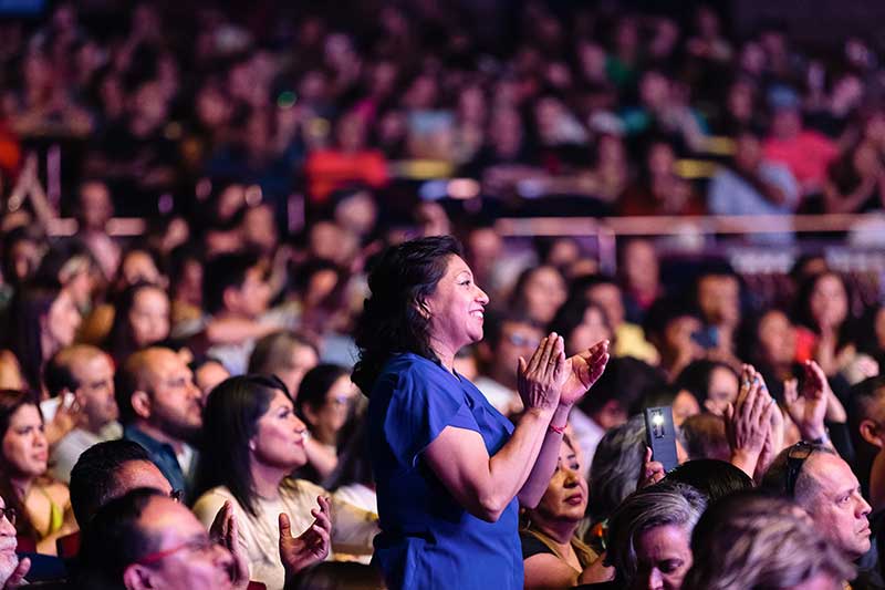 A woman standing in the audience at a performance clapping her hands