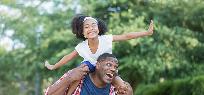 daughter on fathers shoulders outside laughing