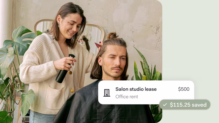 A woman in a cream ribbed cardigan styles a man's shoulder-length hair in a bright, modern salon space with plants and neutral decor. An overlay shows 'Salon studio lease - Office rent $500' with '$115.25 saved' highlighted in green.