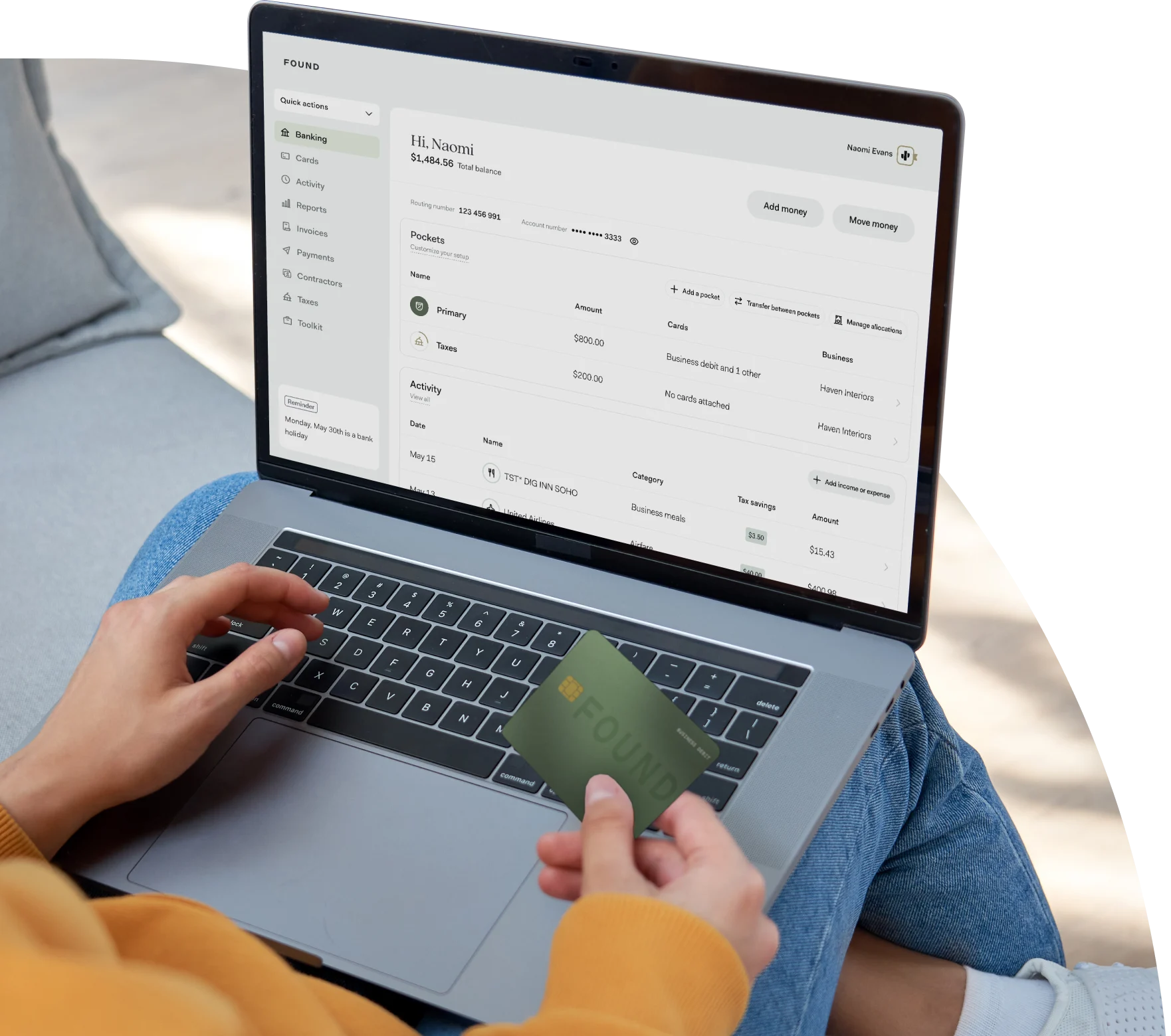 Image of a person with their laptop open on their lap and the Found app open. This person is also holding their Found debit card in their right hand.