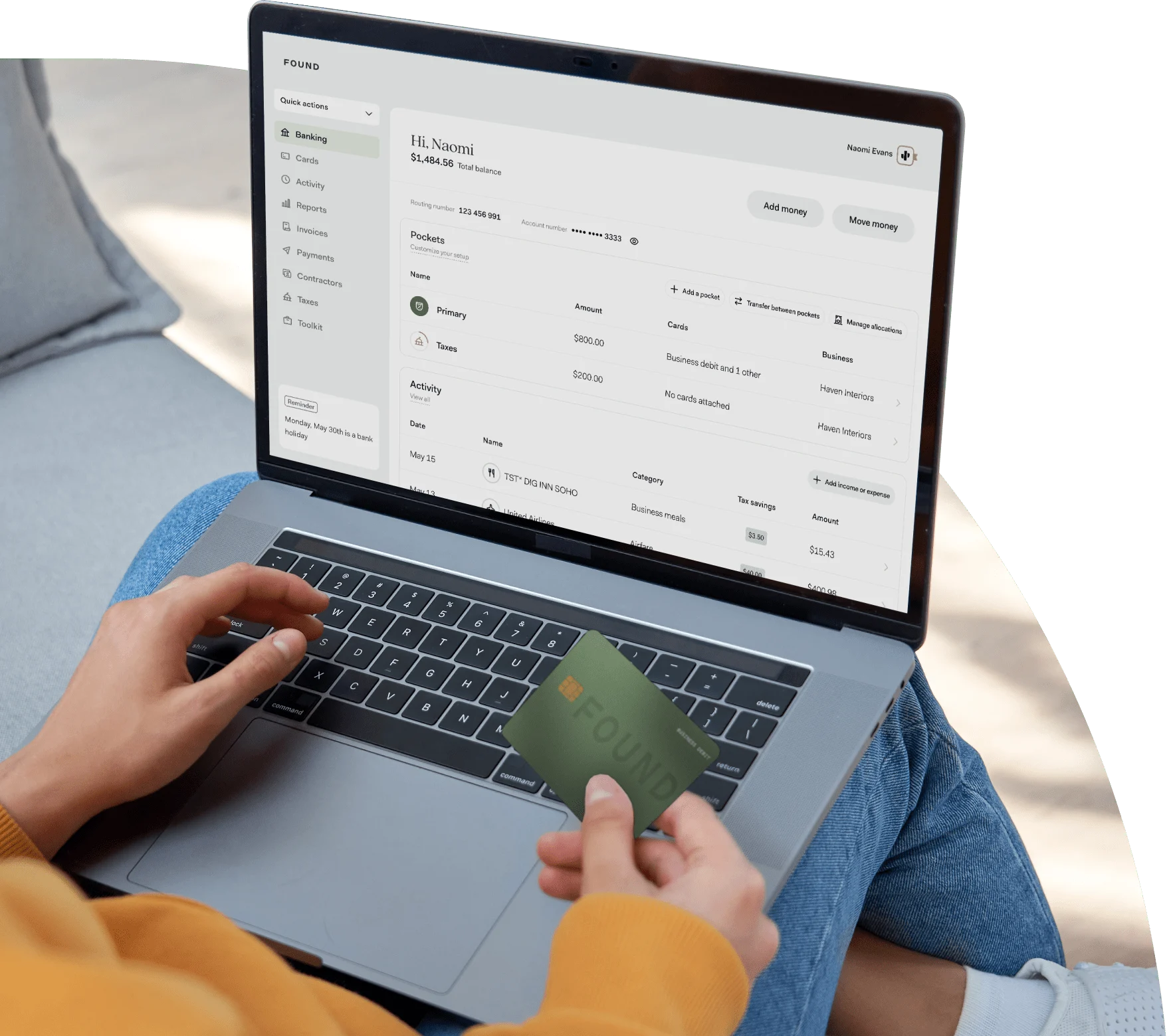 Image of a person with their laptop open on their lap and the Found app open. This person is also holding their Found debit card in their right hand.