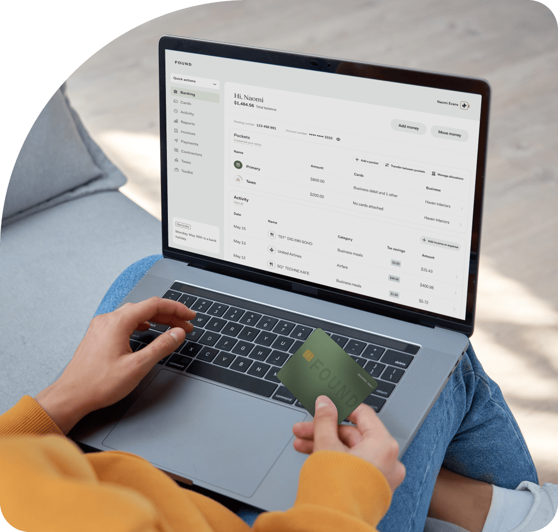 Image of a person with their laptop open on their lap and the Found app open. This person is also holding their Found debit card in their right hand.