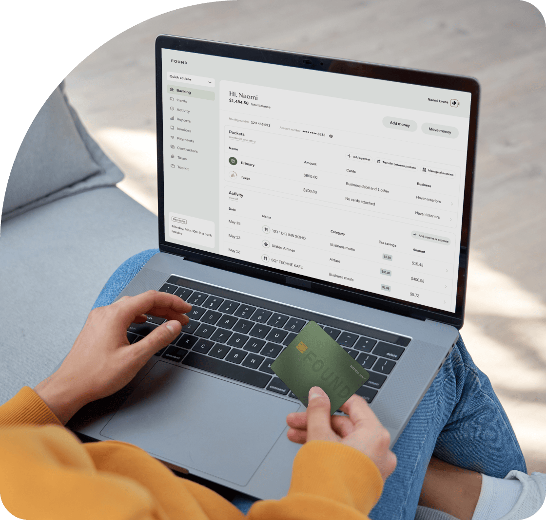 Image of a person with their laptop open on their lap and the Found app open. This person is also holding their Found debit card in their right hand.