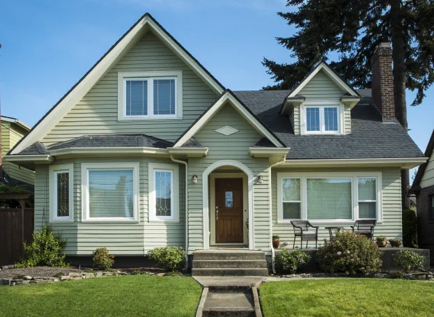 Cape cod-style home with light green paint and manicured lawn