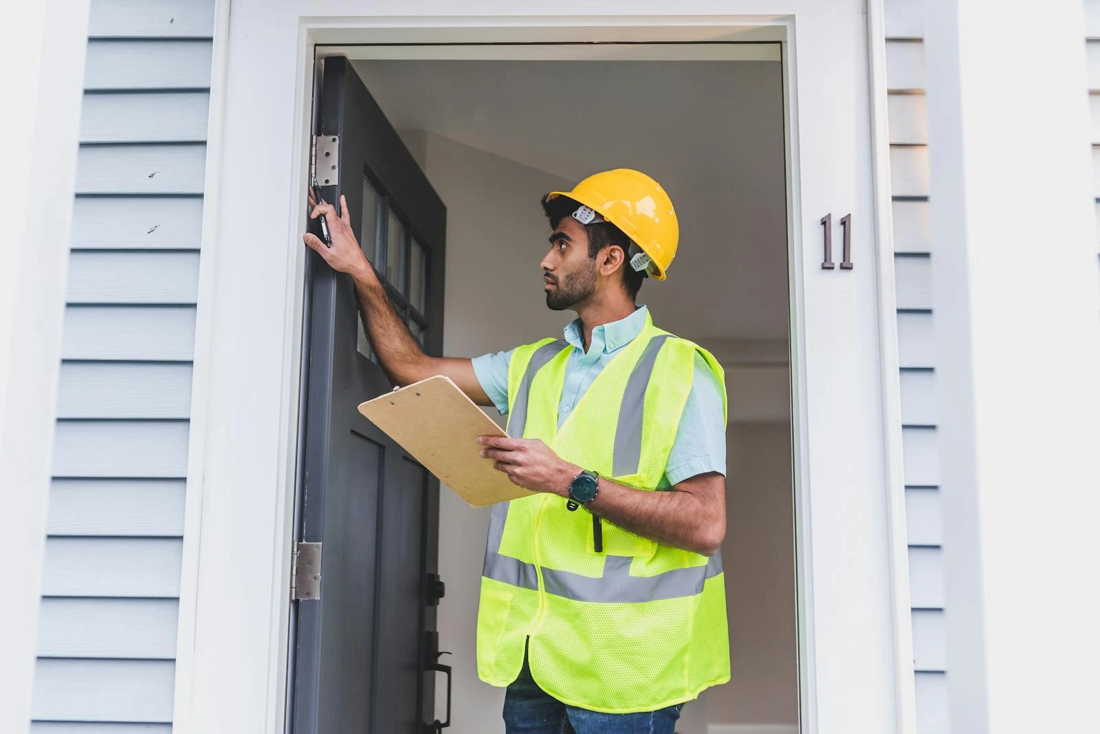 Man in safety vest and a hard hat inspecting the hinges on a door
