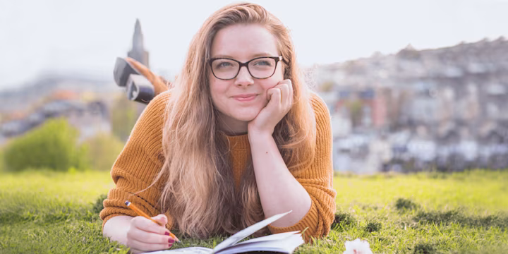 girl laying in the grass writing in her notebook