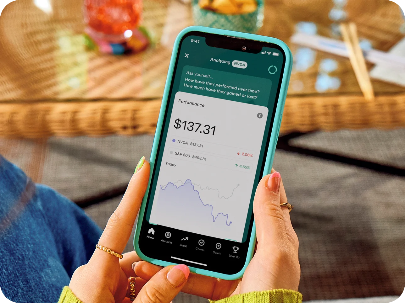 Hands holding teal phone displaying stock performance app showing NVDA at $137.31 and S&P 500 data with performance graph.