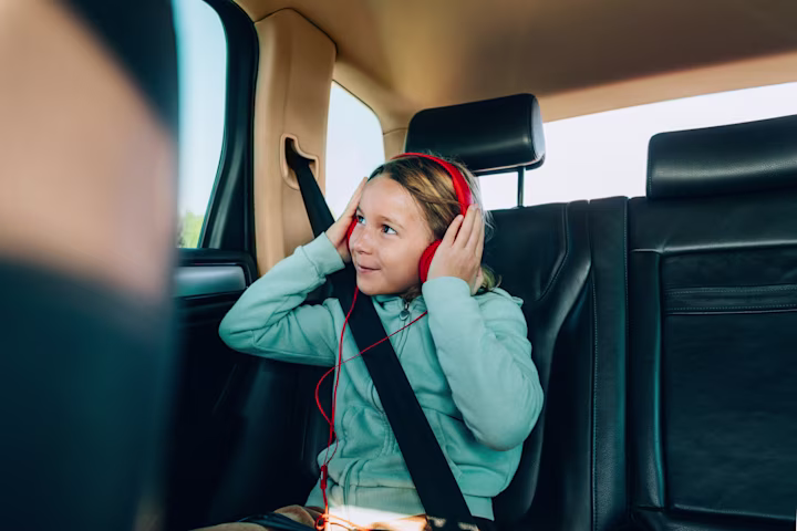 Girl in backseat of car wearing red headphones.
