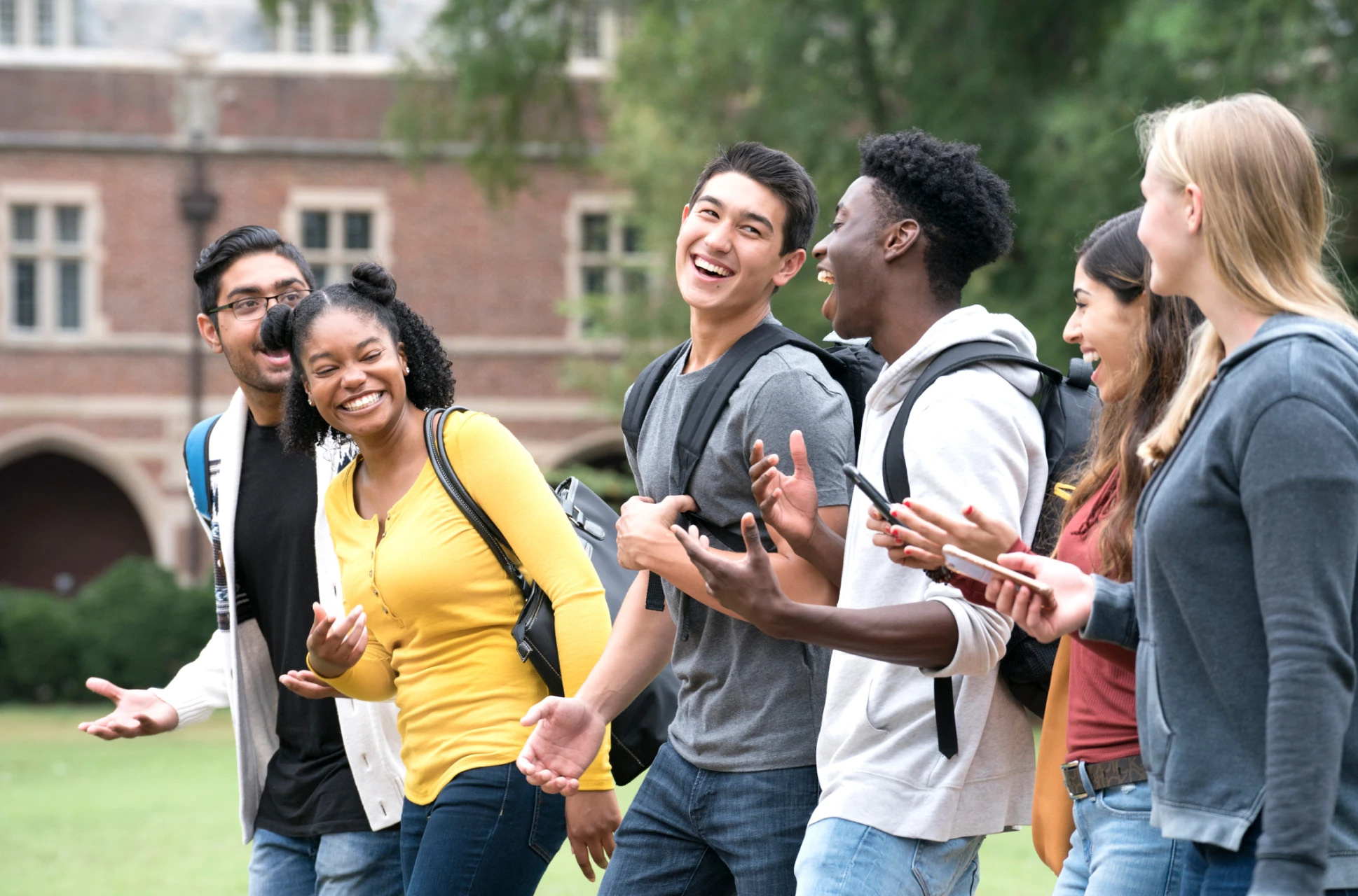 Group of six college students walking together on campus, laughing outside and building a community