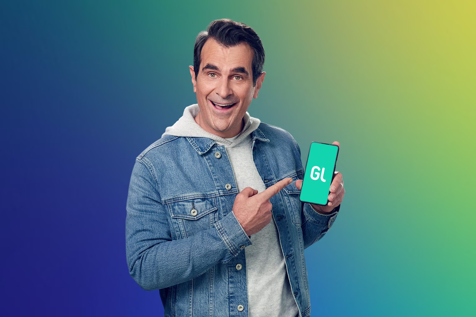ty burrell holding up a smartphone with greenlight money app for families