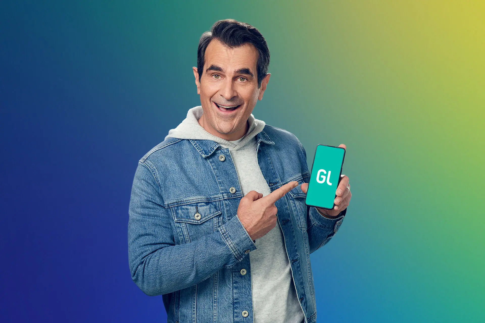 ty burrell holding up a smartphone with greenlight money app for families