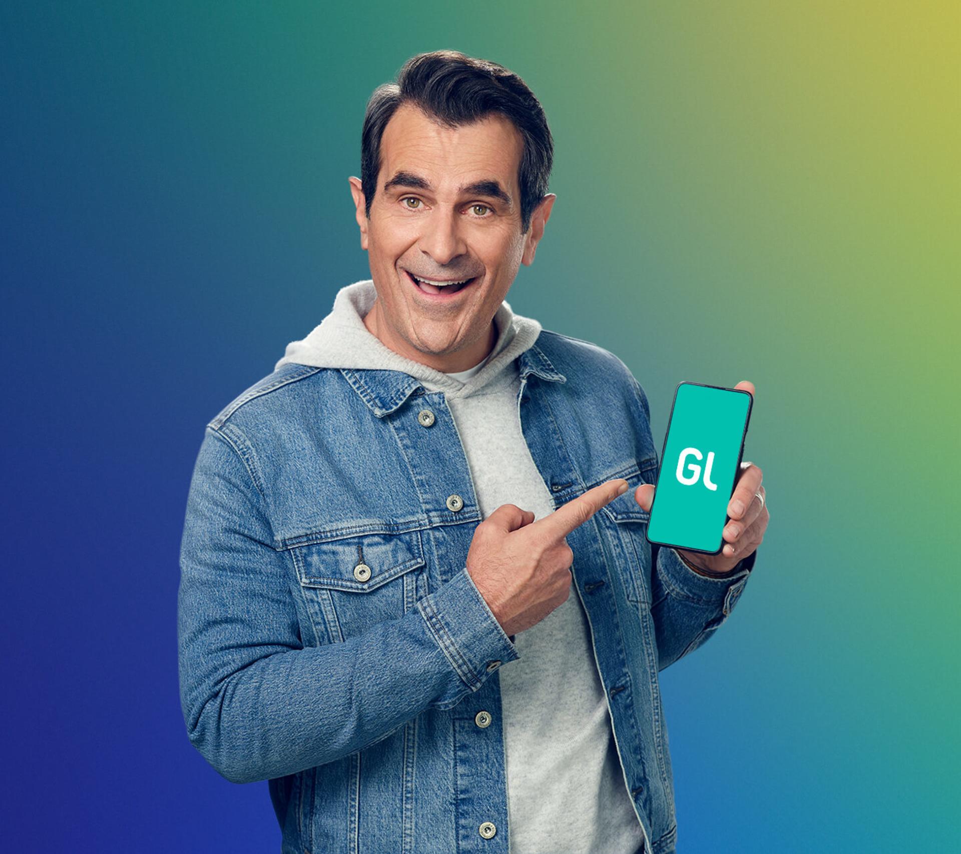 ty burrell holding up a smartphone with greenlight money app for families