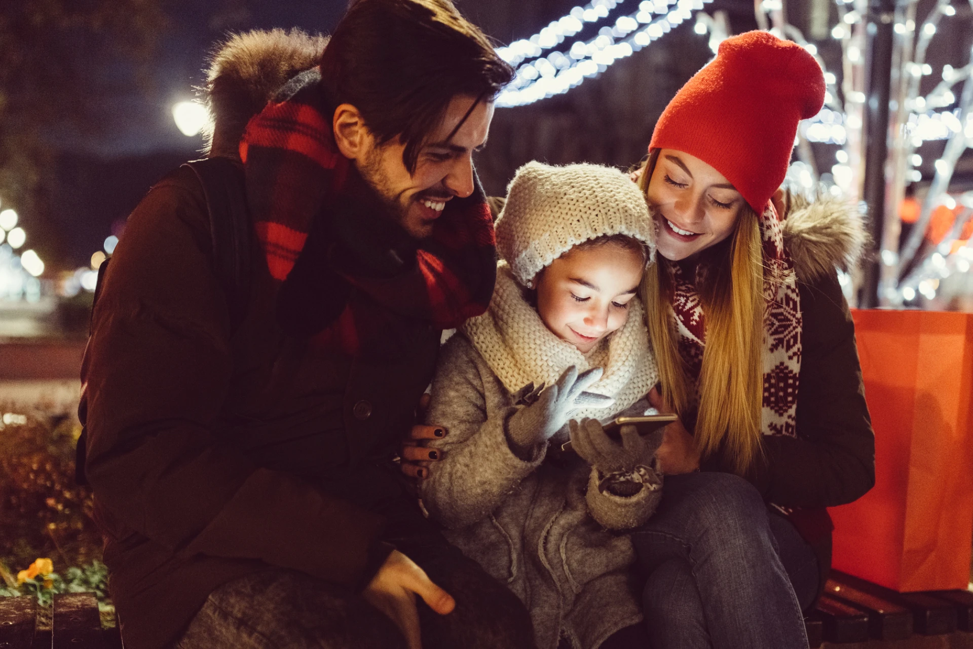 Two parents with daughter outside looking at mobile phone Greenlight app during the holiday winter