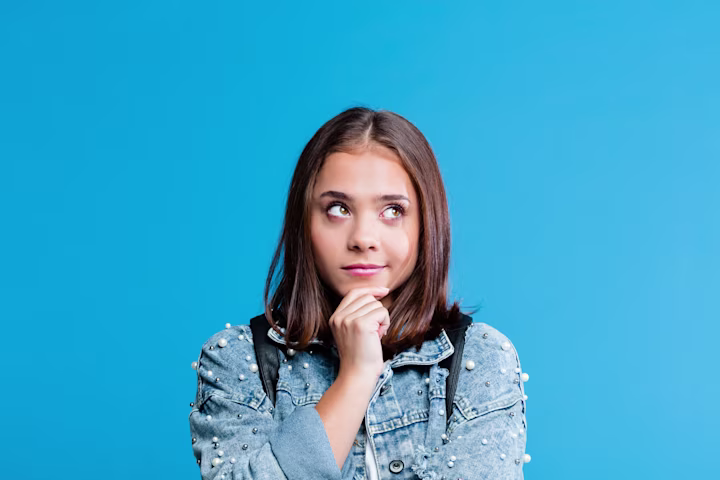 Girl with blue background looking to the side while holding her chin.