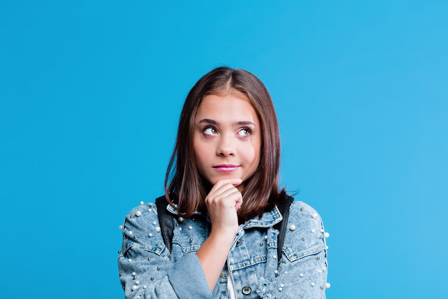 Girl with blue background looking to the side while holding her chin.