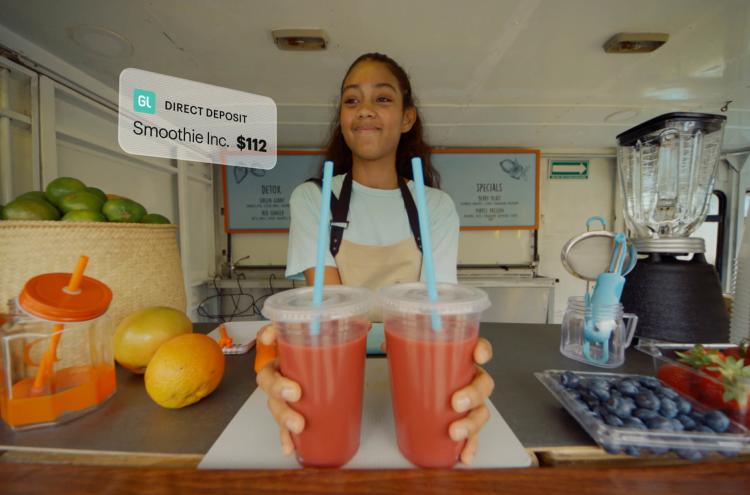 Teen girl working at smoothie shop holding two drinks, gets direct deposit via Greenlight money account