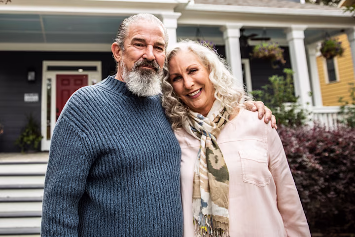 Elderly couple standing together in front of a house.