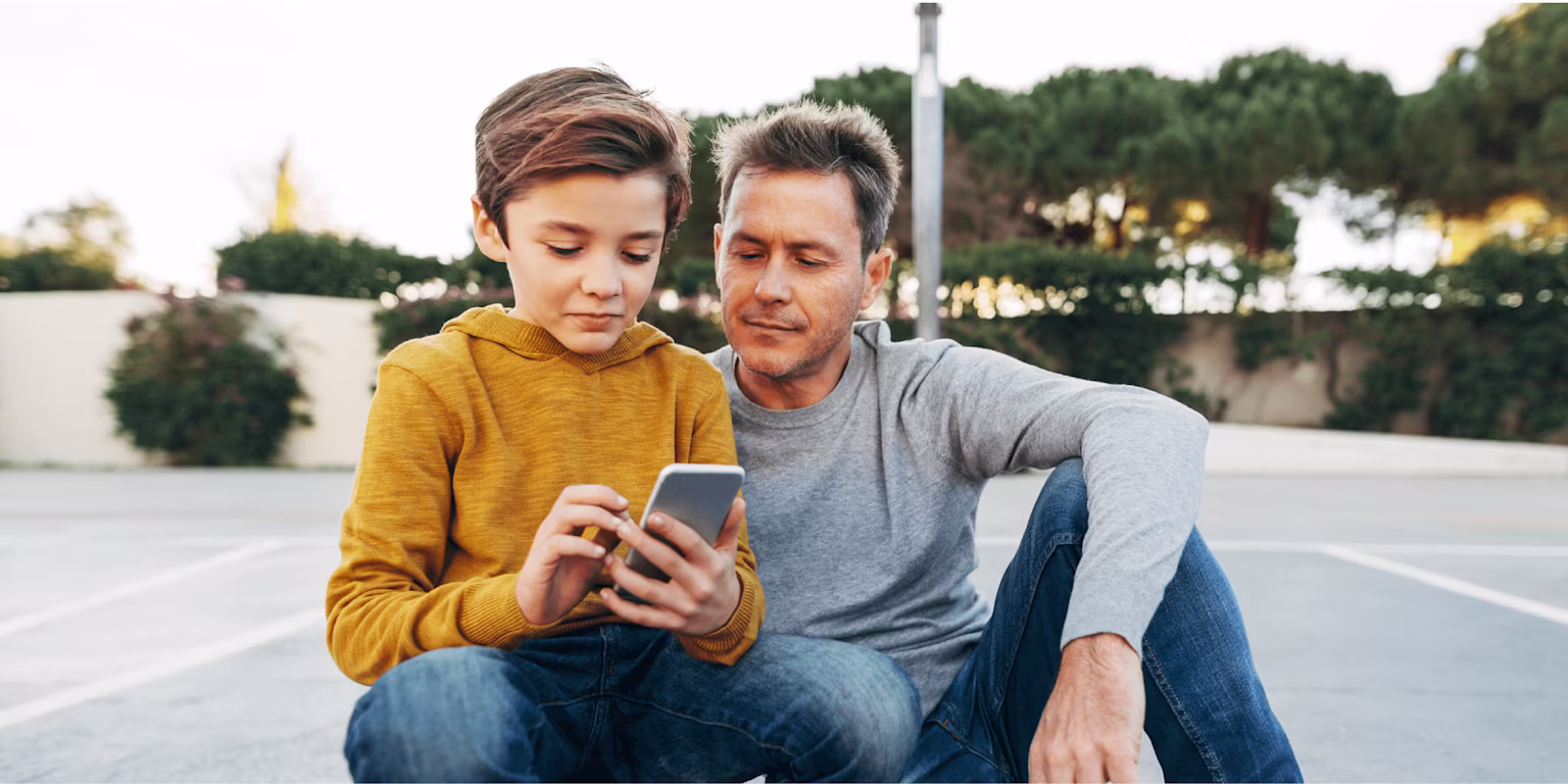 young boy looking at a smartphone next to his father