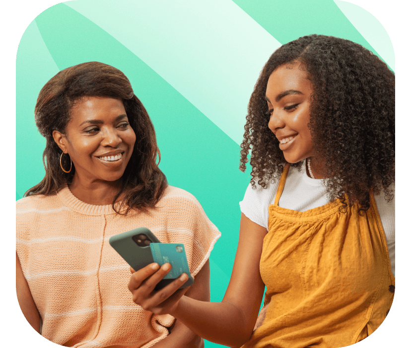 Mother looking at her teenage daughter holding a Greenlight debit card and smartphone