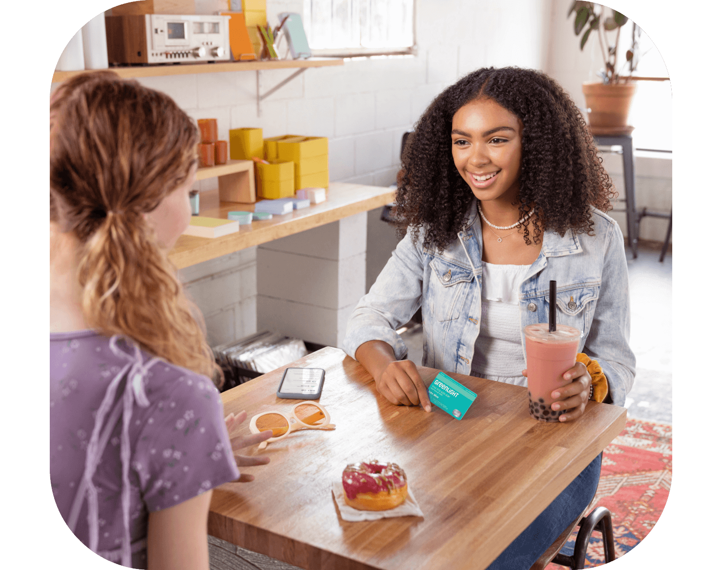 two girls at a table eating, with one holding her Greenlight no hidden fees kids debit card
