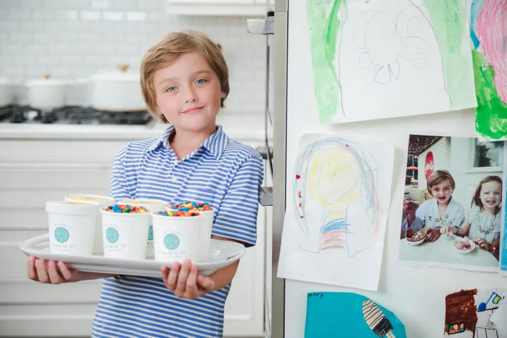young boy standing in his kitchen, holding a tray of tubs filled with M&M's and dough