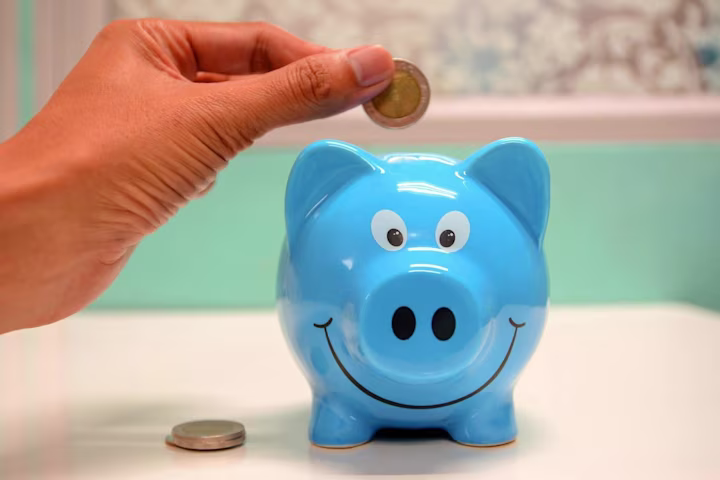A hand putting coins into a blue piggybank.