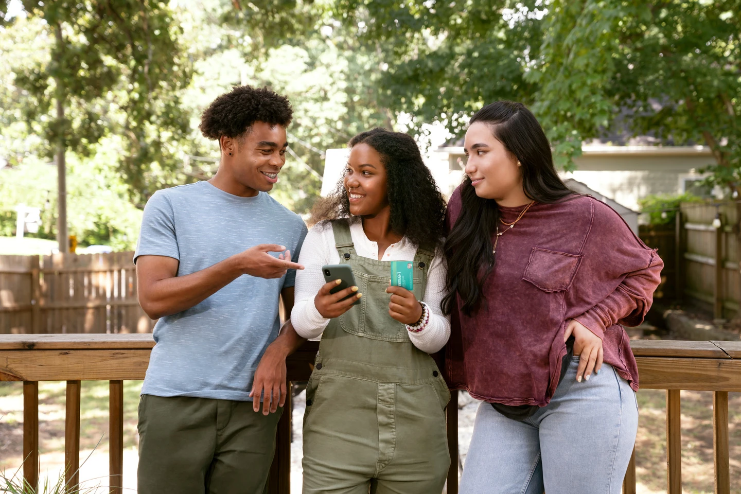 Teens outside hanging in a group of 3 discussing Greenlight card and debit card with Savings app