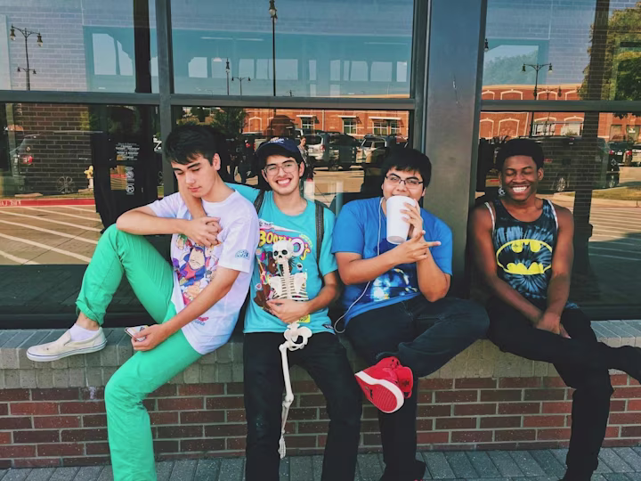 A group of teenage boys hanging out outside smiling at the camera.