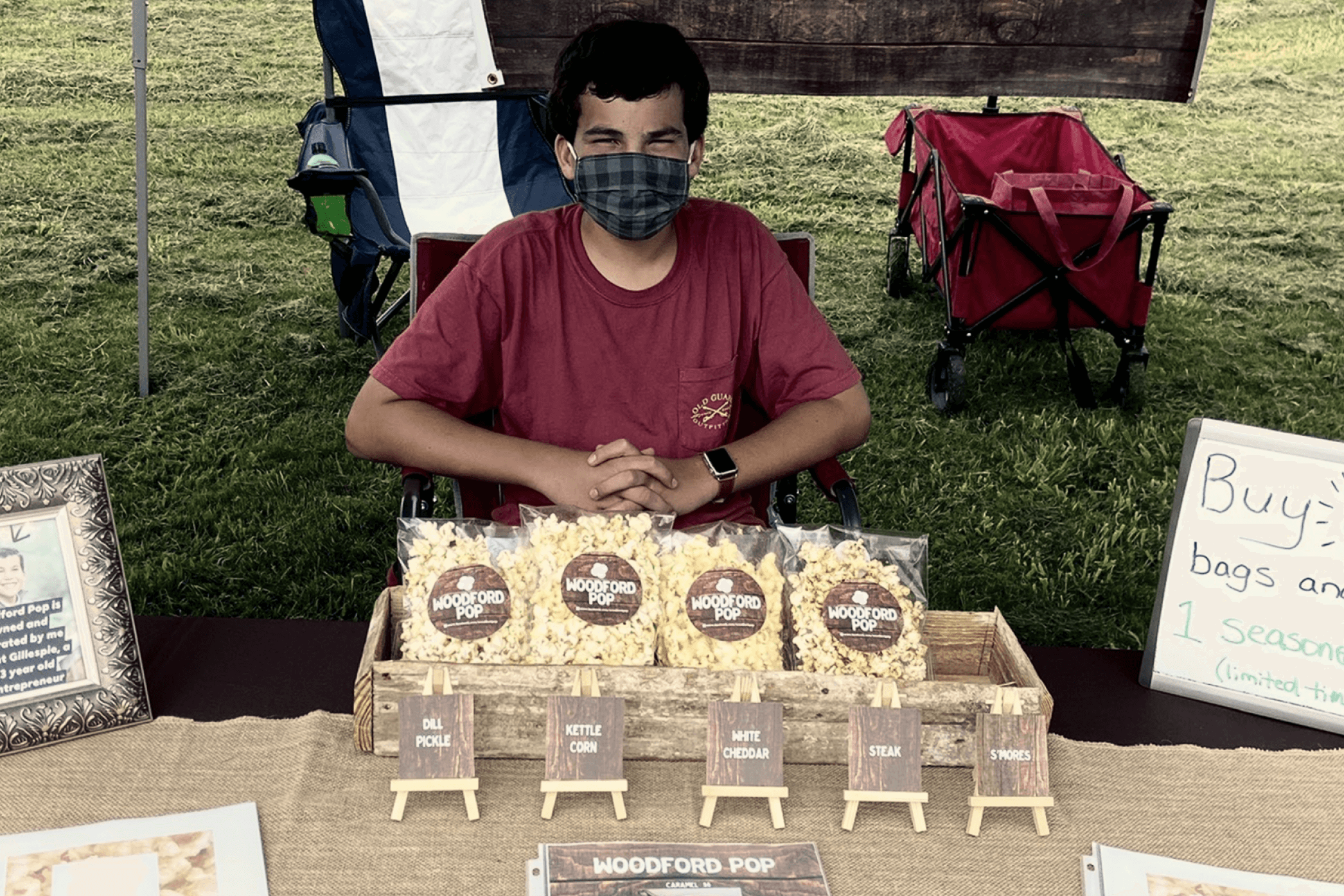 young boy sitting down with a mask on outside selling popcorn