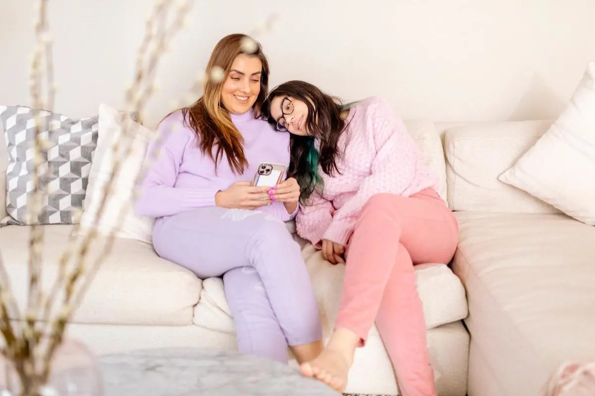 Mother and daughter hanging out on a couch while using a phone