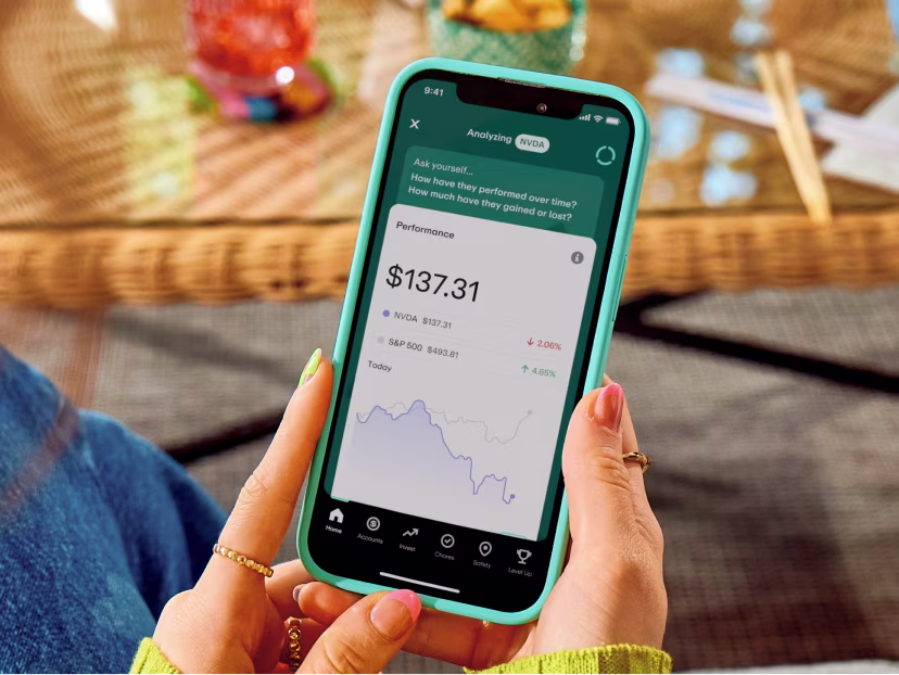Person holding turquoise phone displaying investment app with NVDA stock performance at $137.31 and performance graph.