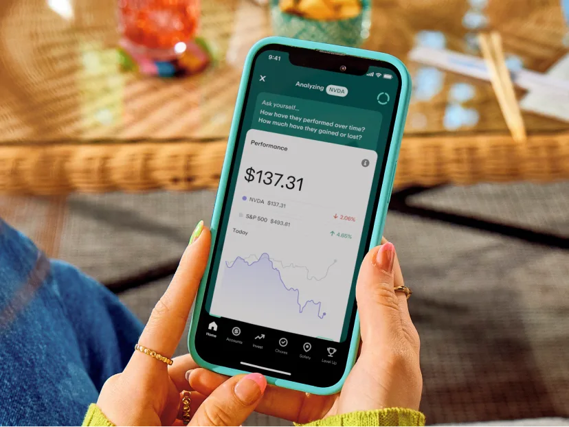 Person holding turquoise phone displaying investment app with NVDA stock performance at $137.31 and performance graph.