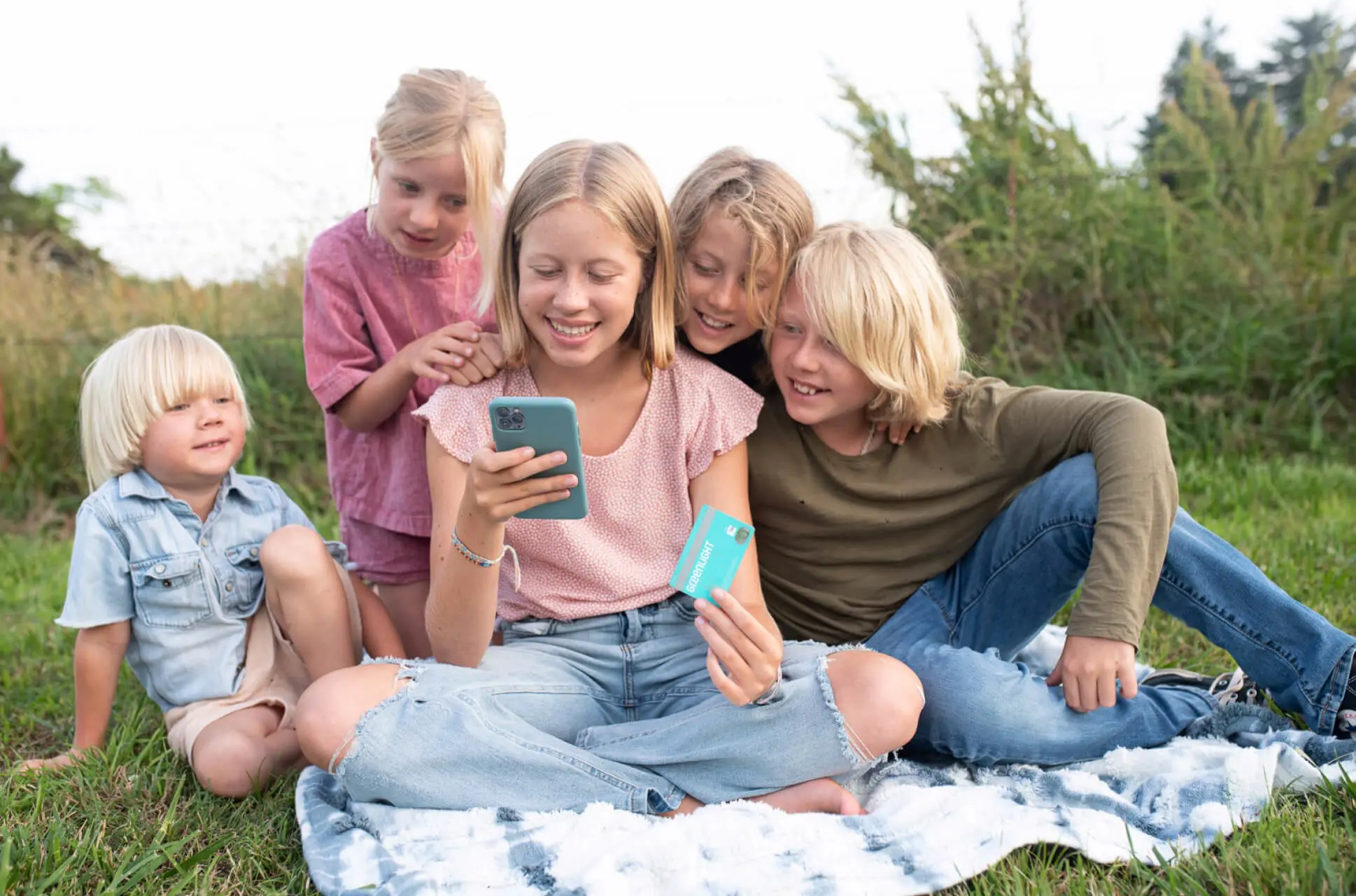 Five siblings outside on the grass playing financial literacy games with Greenlight's money app