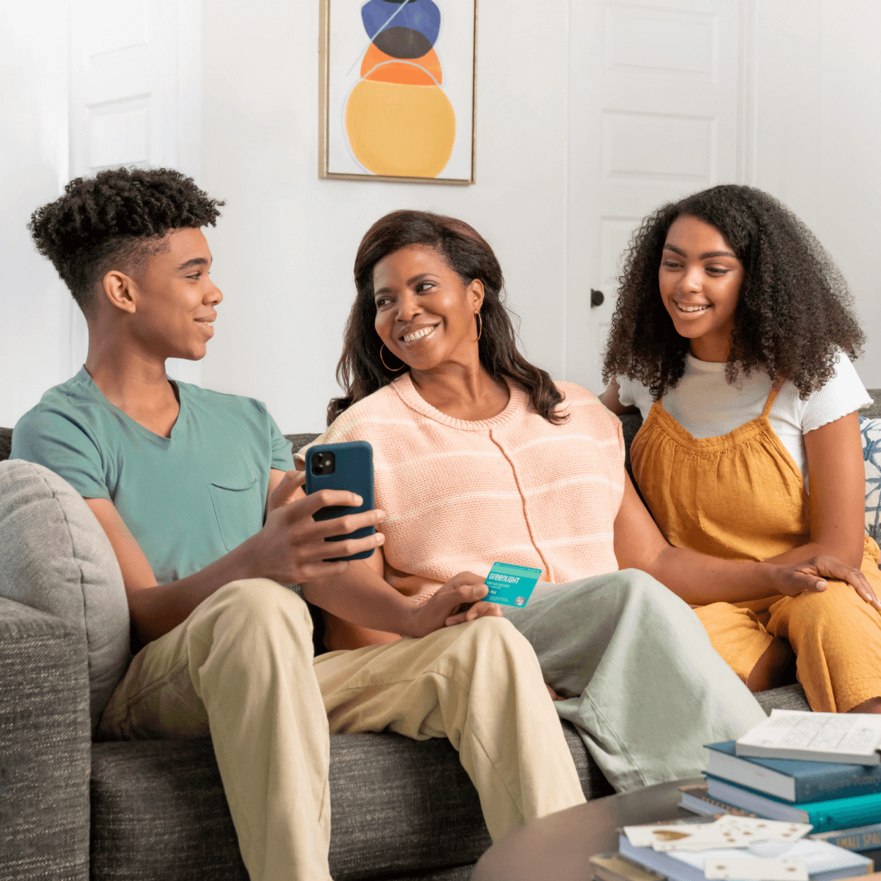 teenage son holding a smartphone and greenlight debit card with mother and teen girl