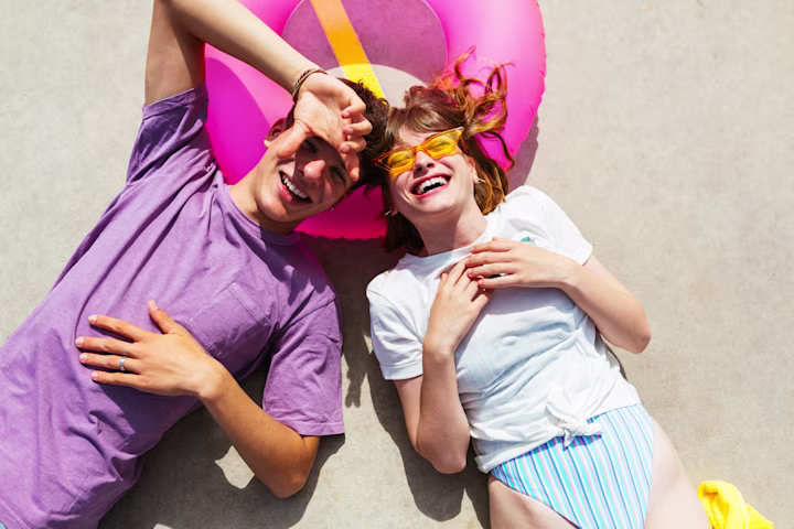 A boy and girl laying on a pool floating with summer clothes on. 