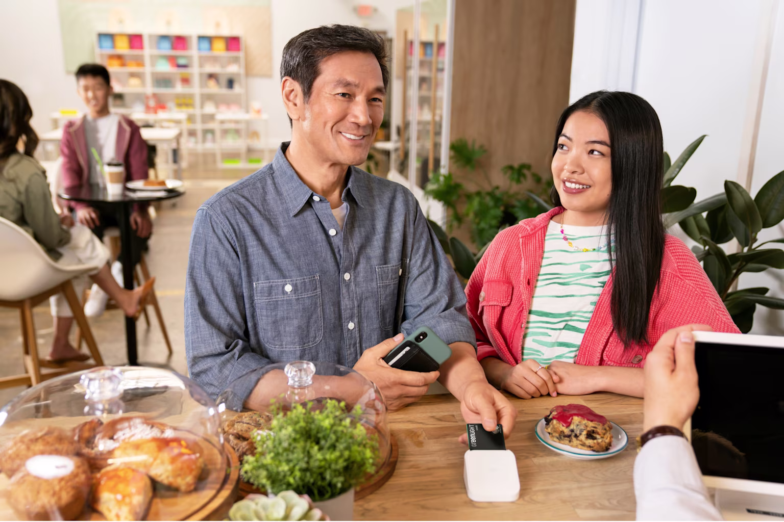 Father and daughter paying with their Greenlight parent credit card at a coffee shop while similing