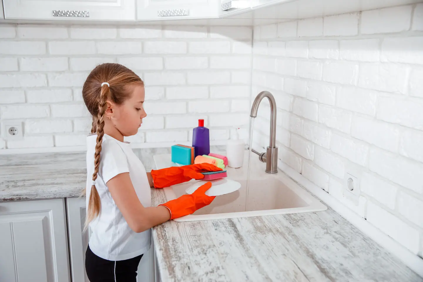 Chores for 7-year-olds: A young girl washes a dish with a sponge in the kitchen