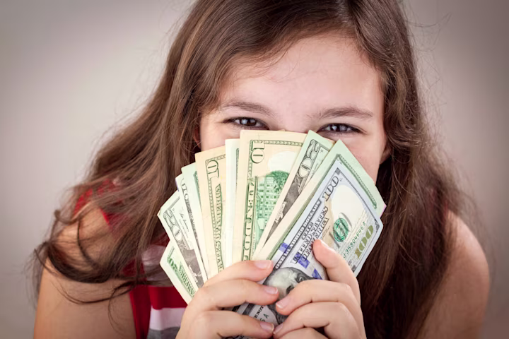 Financial literacy for teens: girl happily covering her face with money