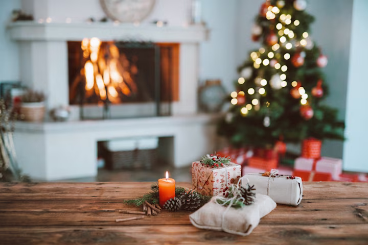 A christmas tree decorated next to a fireplace and presents. 