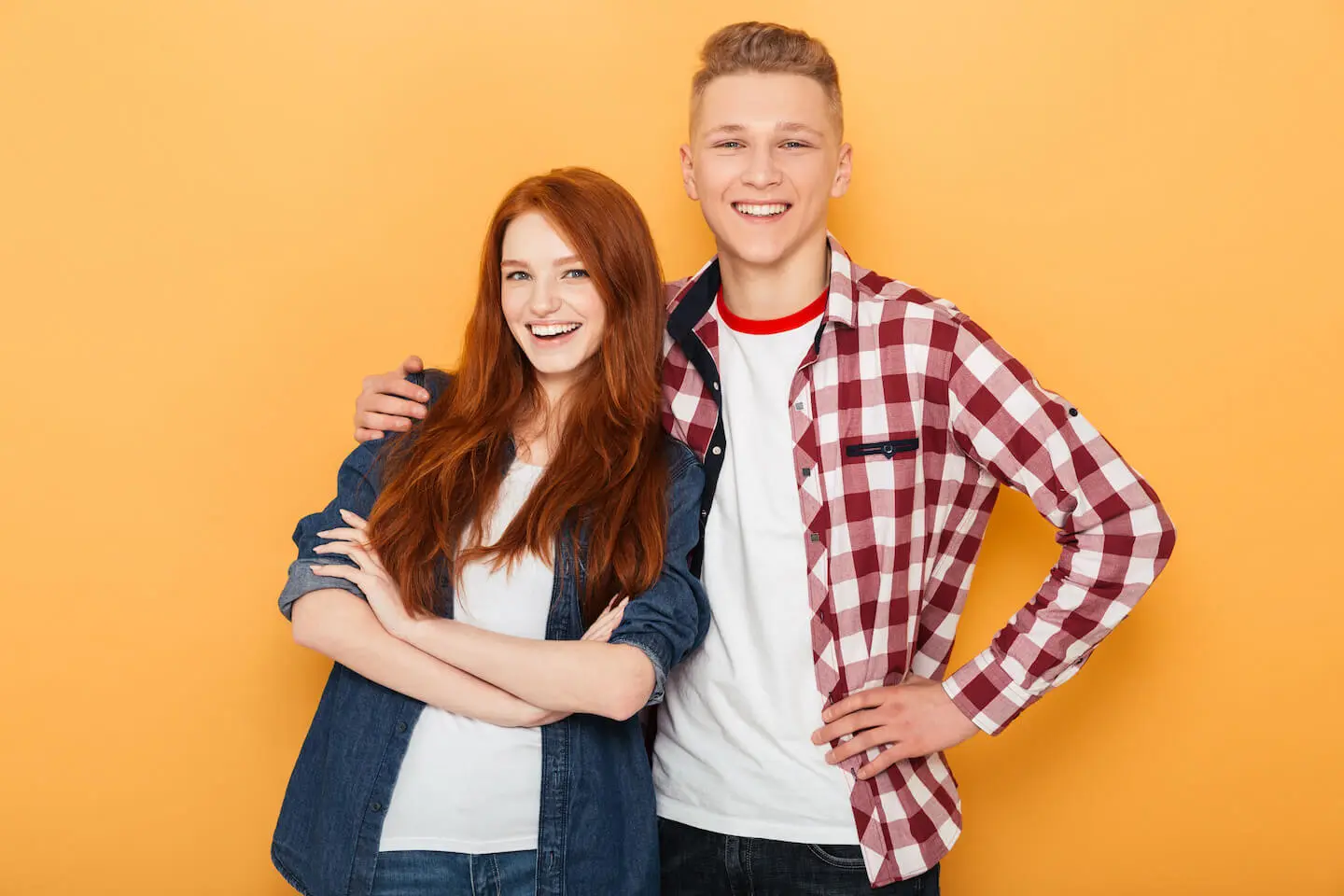 Two smiling teens stand together in front of an orange background