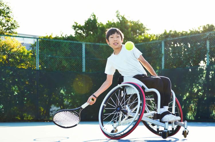 Young teen on wheelchair coaching and playing tennis while earning money for his Greenlight Savings Goals