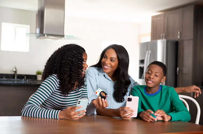 Mom sits with her two children and uses the Greenlight debit card and app to teach her kids about investing