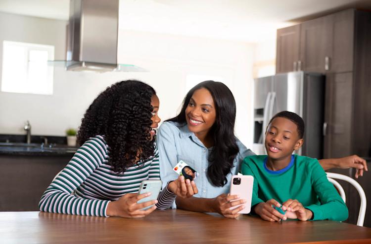 Mom sits with her two children and uses the Greenlight debit card and app to teach her kids about investing