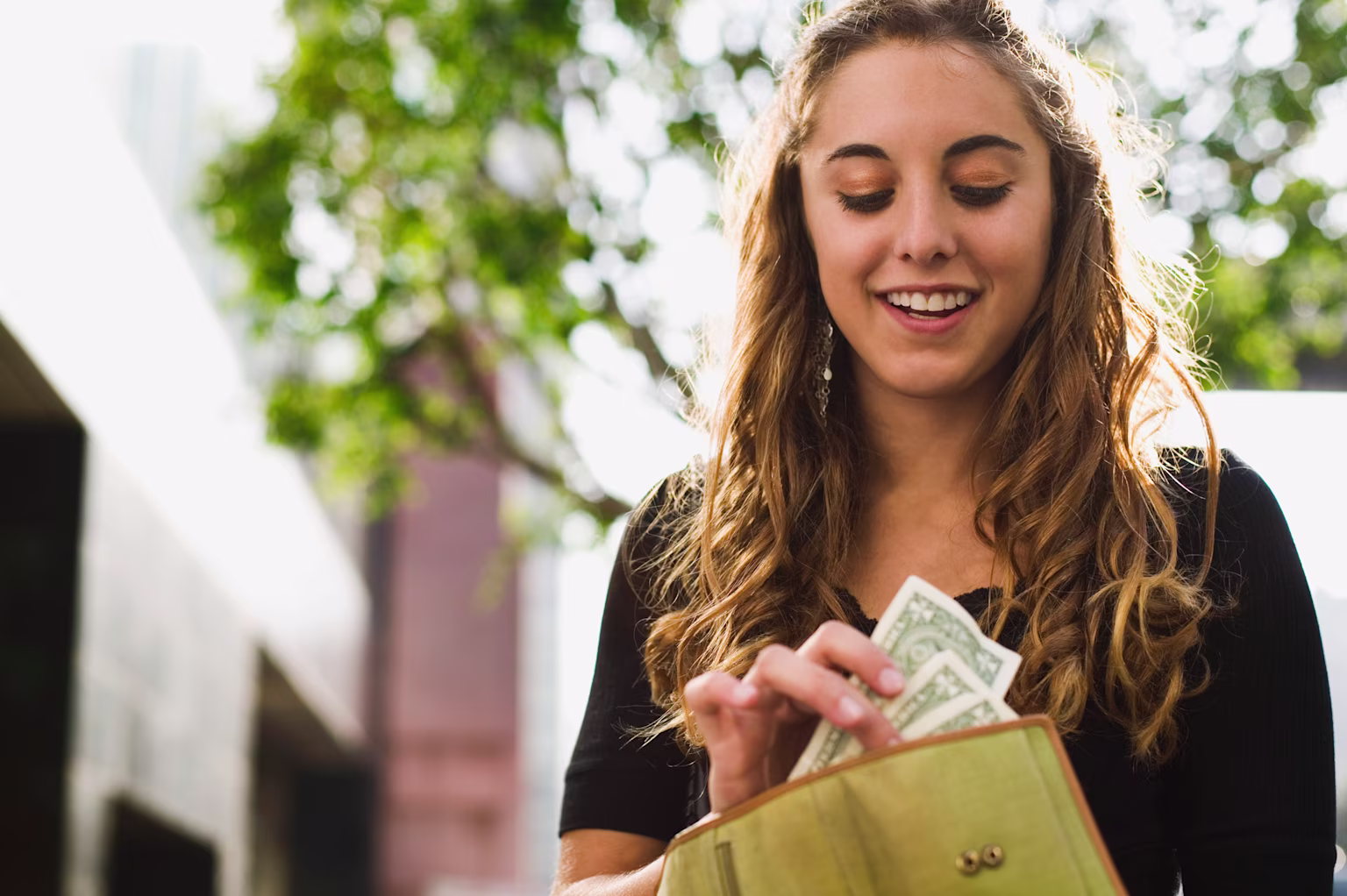 Woman standing outside and putting cash in her wallet.