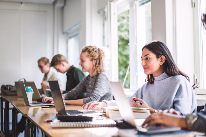 blog 1920x1280 static header - Teen girl researching college options in a classroom using her laptop with other students