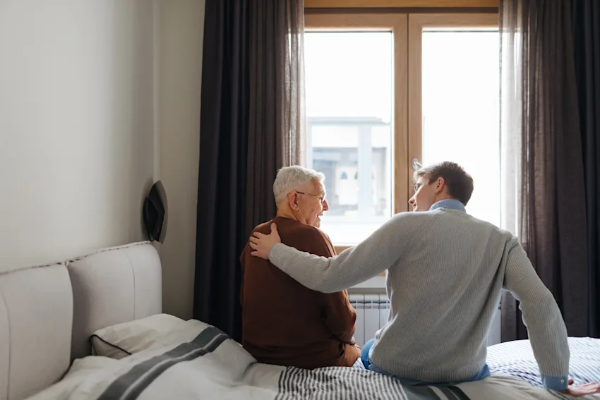 Elderly father and son sitting on bed talking