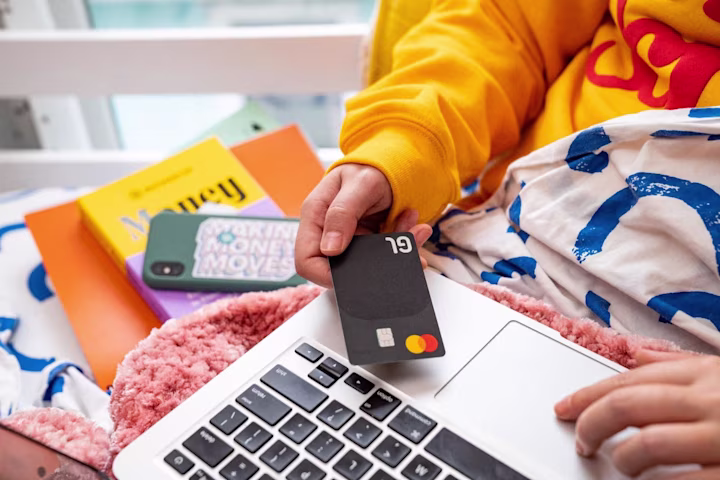 A person sitting on their bed with a laptop and a credit card in hand.